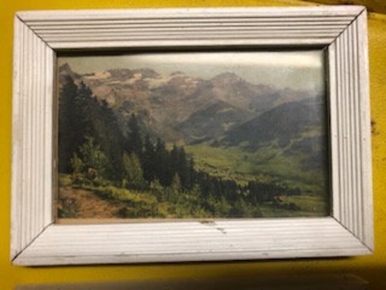 Peut inclure: Une photographie vintage encadr&eacute;e d'une vall&eacute;e de montagne avec des sommets enneig&eacute;s en arri&egrave;re-plan. La photo est dans un cadre en bois blanc au design simple.