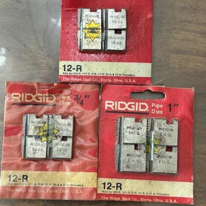 May include: Three red RIDGID pipe die packages, labeled 1/2", 3/4", and 1", with silver dies. Each package has the "RIDGID" logo and "12-R" model number. The dies are marked "High Speed" and "H.S."