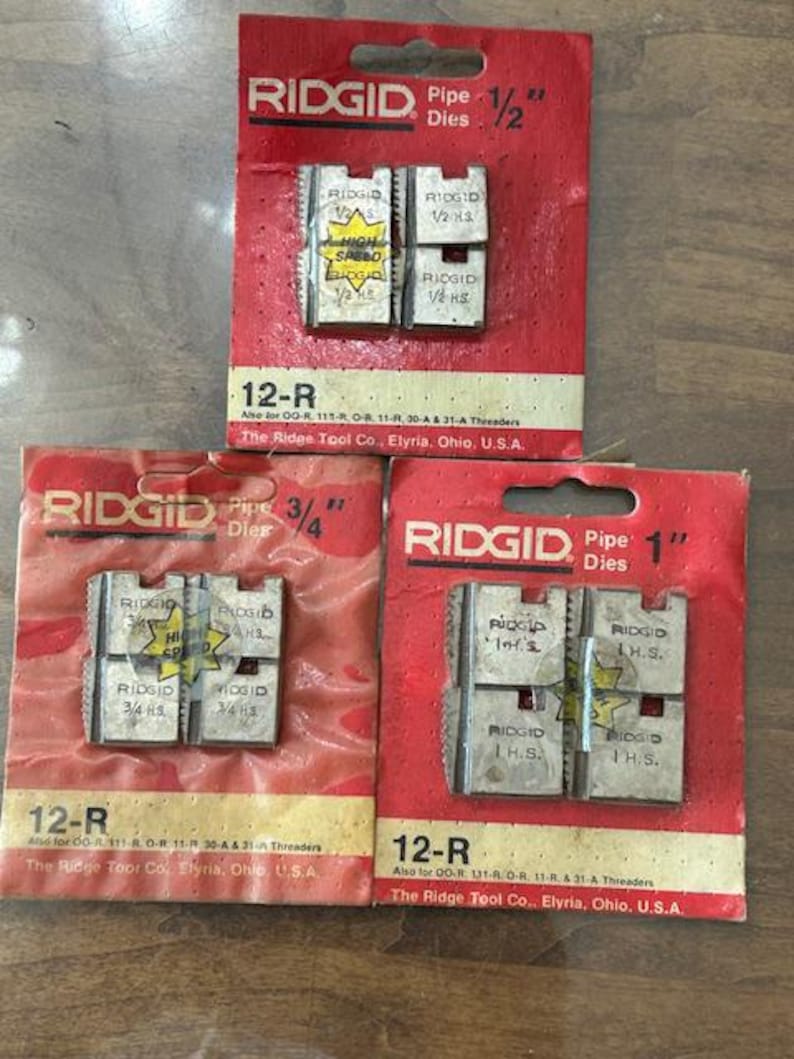 May include: Three red RIDGID pipe die packages, labeled 1/2", 3/4", and 1", with silver dies. Each package has the "RIDGID" logo and "12-R" model number. The dies are marked "High Speed" and "H.S."