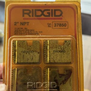 May include: A Ridgid 2" NPT pipe die set in a clear plastic package. The package has an orange label with the Ridgid logo and product information. The die set includes four metal dies.