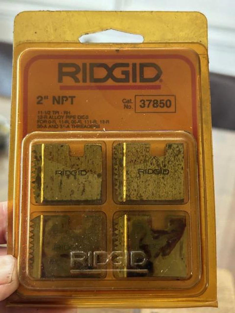 May include: A Ridgid 2" NPT pipe die set in a clear plastic package. The package has an orange label with the Ridgid logo and product information. The die set includes four metal dies.