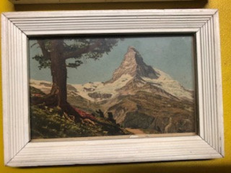 Peut inclure: Une estampe vintage encadr&eacute;e repr&eacute;sentant un paysage de montagne avec un sommet enneig&eacute; et un arbre au premier plan.