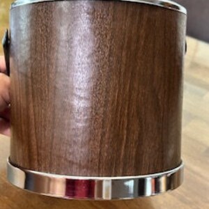 May include: A brown wooden ice bucket with a silver lid and handles. The bucket has a silver band around the top and bottom.