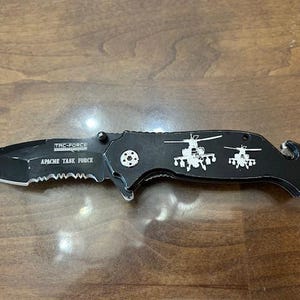 May include: Black folding knife with a serrated edge and the text "TAC-FORCE APACHE TASK FORCE". The handle features two helicopter graphics. Includes a bottle opener and a small metal loop.