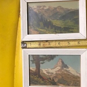 Peut inclure: Deux estampes vintage encadr&eacute;es repr&eacute;sentant des paysages de montagne suisse. L'estampe du haut montre une vall&eacute;e avec des montagnes enneig&eacute;es en arri&egrave;re-plan. L'estampe du bas montre un sommet de montagne avec un arbre au premier plan.