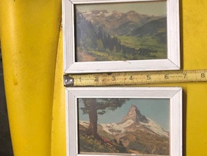 Peut inclure: Deux estampes vintage encadr&eacute;es repr&eacute;sentant des paysages de montagne suisse. L'estampe du haut montre une vall&eacute;e avec des montagnes enneig&eacute;es en arri&egrave;re-plan. L'estampe du bas montre un sommet de montagne avec un arbre au premier plan.