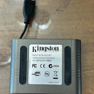 May include: A gray Kingston Technology external hard drive with a black USB cable attached. The device has a white label with black text, including the Kingston logo, part number, and other technical specifications. The USB cable is black.