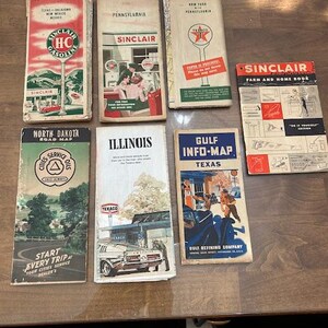 May include: A collection of vintage road maps and booklets, featuring brands like Sinclair, Texaco, and Gulf. The maps showcase state-specific information, with colorful illustrations and retro designs. The collection includes a Sinclair Farm and Home Book.