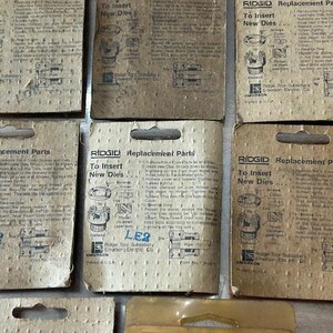 May include: A collection of vintage RIDGID replacement parts packaging. The cardboard packaging is tan with black text and illustrations. The text includes "To Insert New Dies" and "LE2". The packaging is for Ridge Tool Subsidiary Emerson Electric Co.