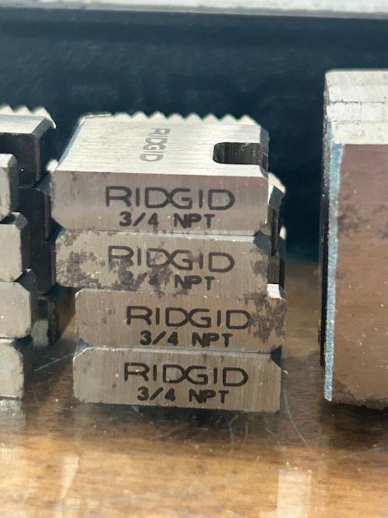 May include: Close-up of several metal RIDGID 3/4 NPT die heads. The die heads are stacked and have the RIDGID logo and size information printed on them. The metal has a slightly worn appearance.