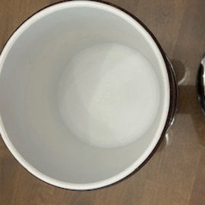 May include: Empty white ceramic ice bucket with a silver lid. The bucket has a black rim and a black stripe around the top.