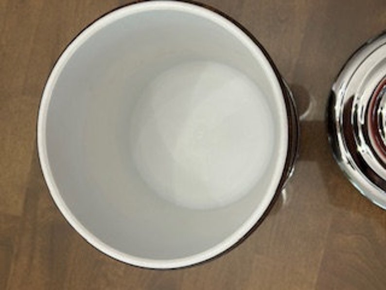 May include: Empty white ceramic ice bucket with a silver lid. The bucket has a black rim and a black stripe around the top.