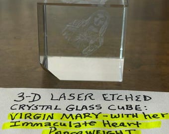 May include: A clear 3-D laser etched crystal glass cube paperweight featuring the Virgin Mary with her Immaculate Heart. The cube measures 1/2 inch tall by 1/2 inch wide. The text on the paper reads 3-D LASER ETCHED CRYSTAL GLASS CUBE.