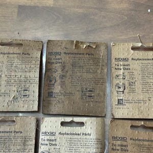 May include: Several vintage RIDGID replacement parts cards are displayed, featuring instructions for inserting new dies. The cards are made of aged cardboard and have a rectangular shape with a hole at the top for hanging.