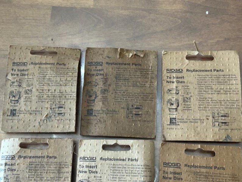 May include: Several vintage RIDGID replacement parts cards are displayed, featuring instructions for inserting new dies. The cards are made of aged cardboard and have a rectangular shape with a hole at the top for hanging.