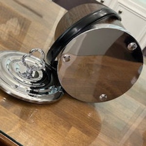 May include: A silver ice bucket with a wooden exterior and a black leather handle. The bucket has a matching lid with a silver knob.