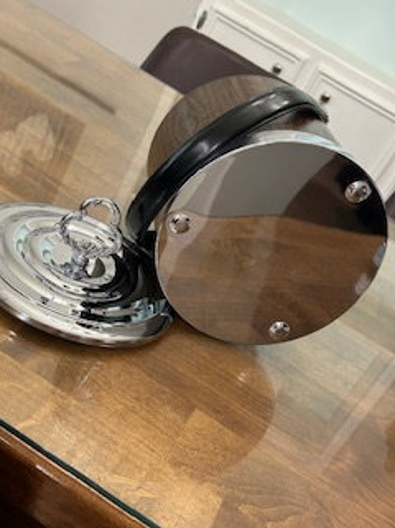 May include: A silver ice bucket with a wooden exterior and a black leather handle. The bucket has a matching lid with a silver knob.
