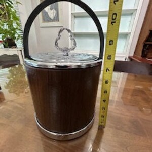 May include: A brown wooden ice bucket with a chrome trim and a silver lid with a crystal handle. The bucket is 9 inches tall.
