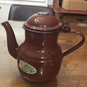 May include: A brown enamel teapot with a lid and a handle. The teapot has a green label with the text "EG" and "Made in Austria" on it.