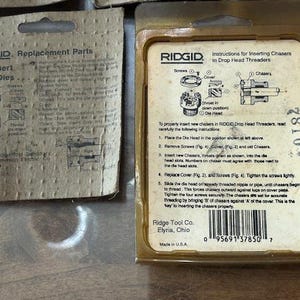 May include: Two vintage RIDGID replacement parts packages. One package is a tan cardboard with instructions for inserting new dies. The other is a clear plastic package with instructions for inserting chasers in drop head threaders.