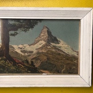 Peut inclure: Une estampe vintage encadr&eacute;e repr&eacute;sentant un paysage de montagne avec un sommet enneig&eacute;, un arbre vert et un premier plan rocheux.