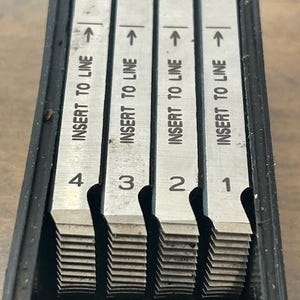 May include: A set of four metal measuring tools with the text "INSERT TO LINE" and numbers 1 through 4. Each tool has an arrow pointing upwards. The tools are in a black case.