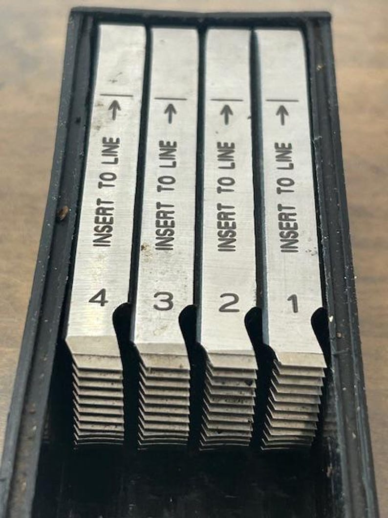 May include: A set of four metal measuring tools with the text "INSERT TO LINE" and numbers 1 through 4. Each tool has an arrow pointing upwards. The tools are in a black case.