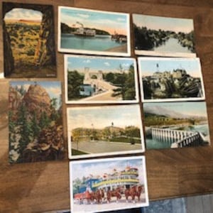 May include: Collection of vintage postcards featuring scenic views of a river, a bridge, a mountain, and a steamboat. The postcards are in various colors and have a faded look.