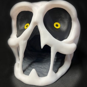 May include: White plastic skull with a large open mouth and black eyes with yellow pupils.