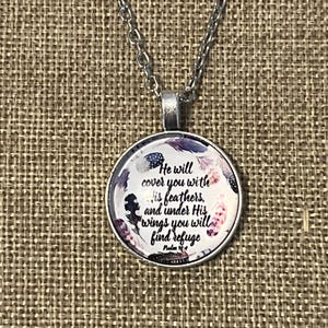 Puede incluir: Un collar de plata con un colgante redondo de vidrio con un dise&ntilde;o floral y el texto "He will cover you with His feathers, and under His wings you will find refuge Psalm 91:4".