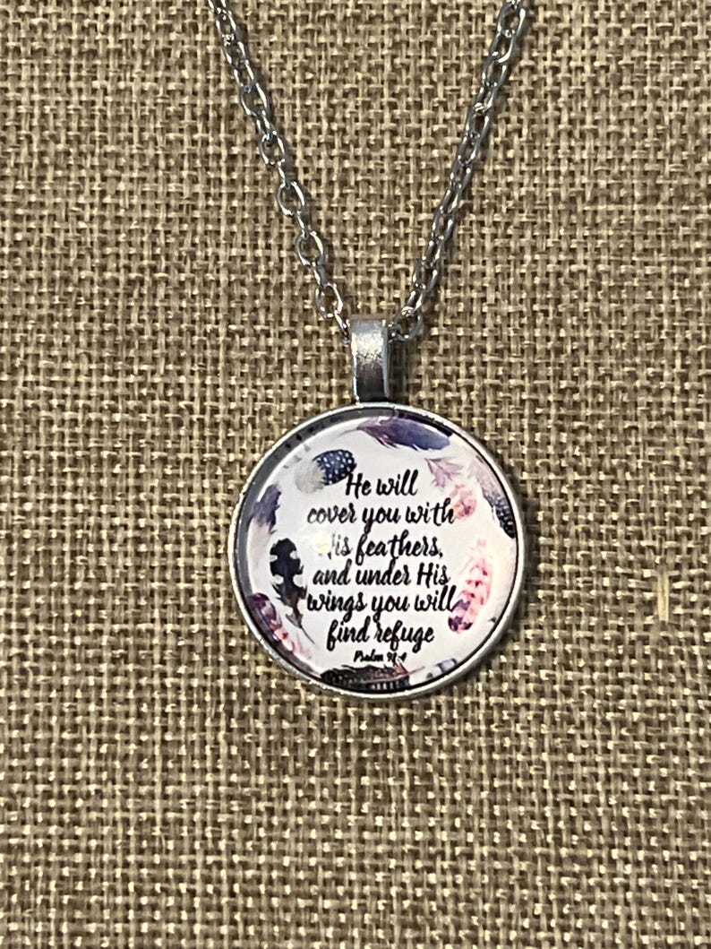 Puede incluir: Un collar de plata con un colgante redondo de vidrio con un dise&ntilde;o floral y el texto "He will cover you with His feathers, and under His wings you will find refuge Psalm 91:4".