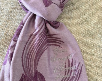 May include: A lavender scarf with a repeating floral pattern in a darker shade of purple. The scarf has a fringed edge and embroidered text that reads "Virtue, Strength & Honor, Proverbs 31."