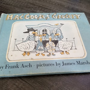 May include: A blue book with the title "Mac Goose's Grocery" and illustrations of geese. The book is by Frank Asch and pictures by James Marshall.