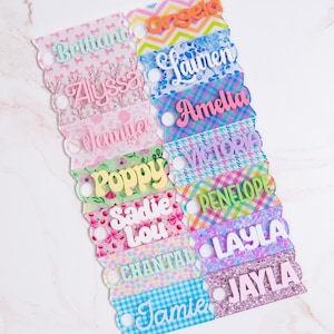 May include: A set of 12 colorful personalized name tags with different patterns. The names include Brittany, Angela, Alyssa, Lauren, Jennifer, Amelia, Poppy, Victoria, Sadie Lou, Penelope, Chantal, Layla, Jamie, and Jayla.