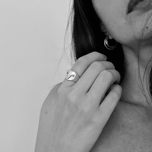 May include: A silver ring with an owl design. The ring is worn on the index finger of a person's hand.