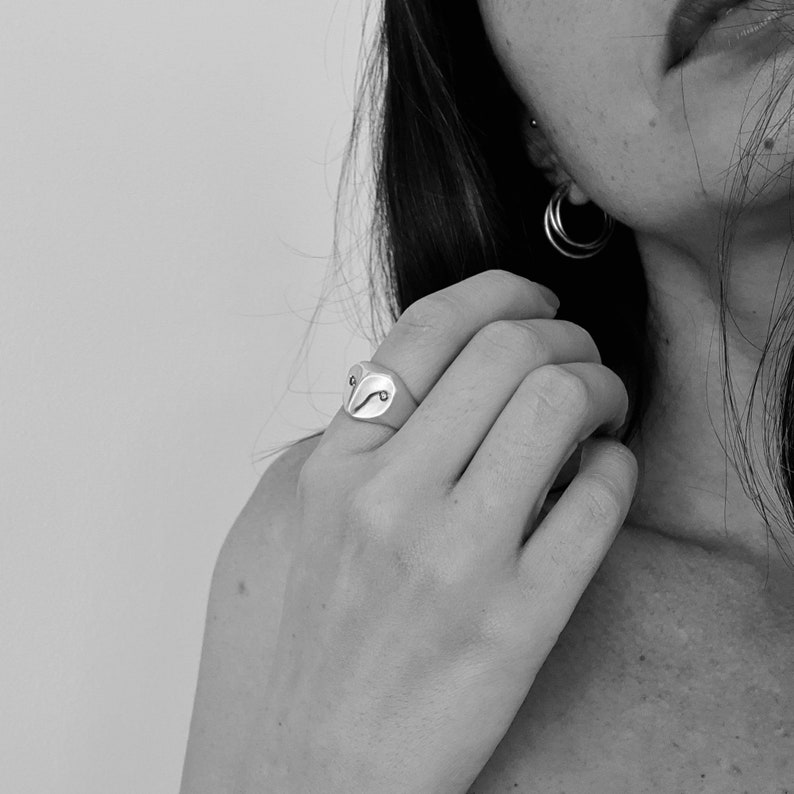 May include: A silver ring with an owl design. The ring is worn on the index finger of a person's hand.