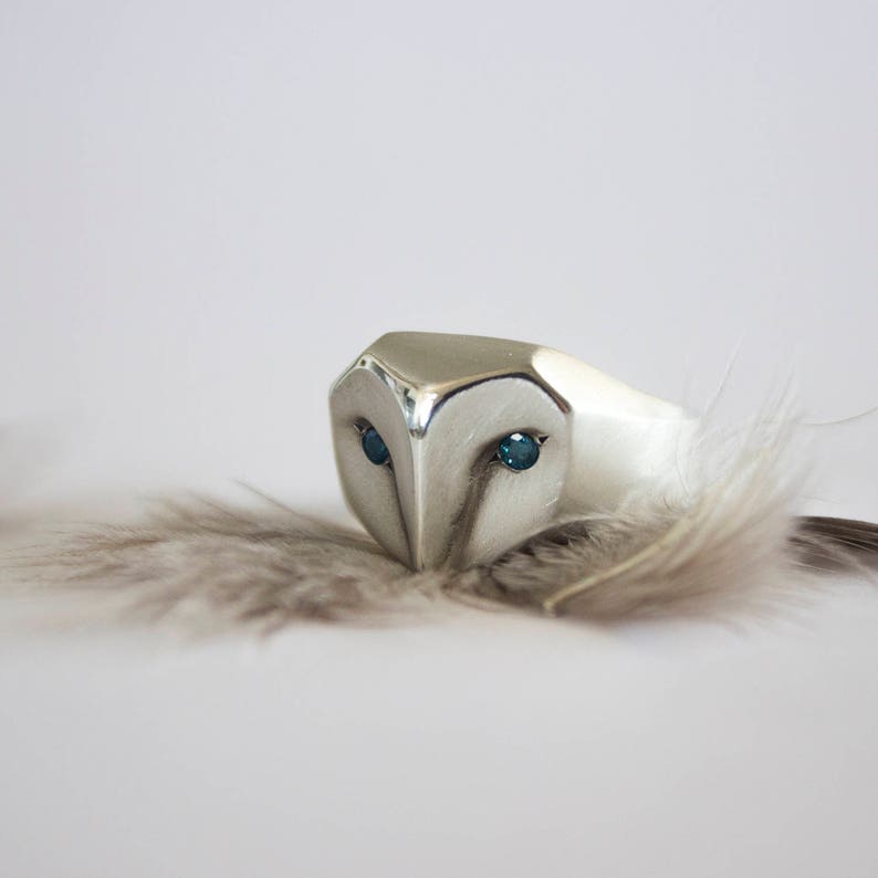 May include: A silver ring shaped like an owl's head with blue gemstone eyes.