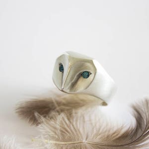 May include: A silver ring with a detailed owl design. The owl's eyes are set with blue gemstones.