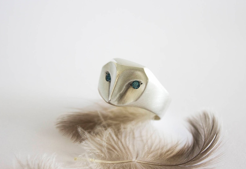 May include: A silver ring with a detailed owl design. The owl's eyes are set with blue gemstones.