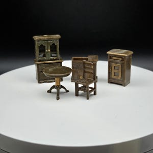 May include: Miniature antique-style furniture set in a bronze finish. The set includes a small round table, a chair, a cabinet with two doors, a cabinet with a single door, and a small cabinet with a drawer.