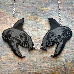 May include: A black necklace with two skull pendants connected by a silver chain. The skulls are detailed and have sharp teeth.