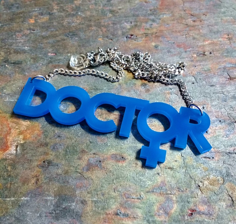 May include: A blue acrylic necklace with the word "DOCTOR" and a female symbol. The necklace is on a silver chain.