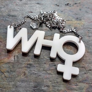May include: A white necklace with a pendant that says "WHO" with a female symbol attached to the "O".