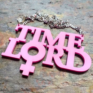 May include: Pink plastic necklace with the words "TIME LORD" and a female symbol.