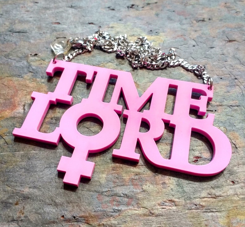 May include: Pink plastic necklace with the words "TIME LORD" and a female symbol.