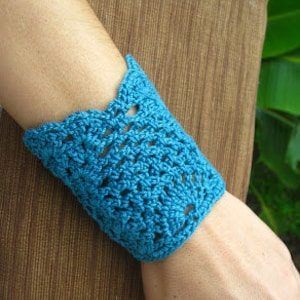 Puede incluir: Un brazalete de ganchillo azul turquesa con un borde festoneado.