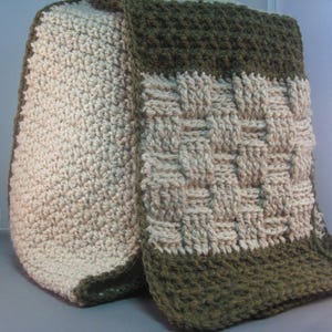 Puede incluir: Una manta de ganchillo de color beige y verde. La manta está hecha con un patrón tejido y tiene un borde de flecos.