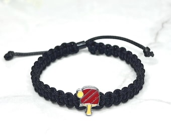 May include: Black braided bracelet with a red and yellow ping pong paddle charm.