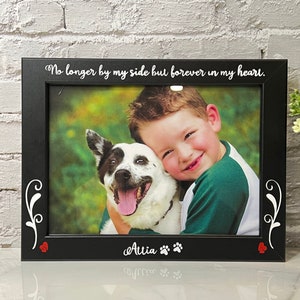 Op de afbeelding: Zwarte fotolijst met een witte inscriptie die luidt: "No longer by my side but forever in my heart." De lijst bevat een foto van een jongen die een hond knuffelt. De inscriptie "Attia" en poot afdrukken bevinden zich onder de foto.