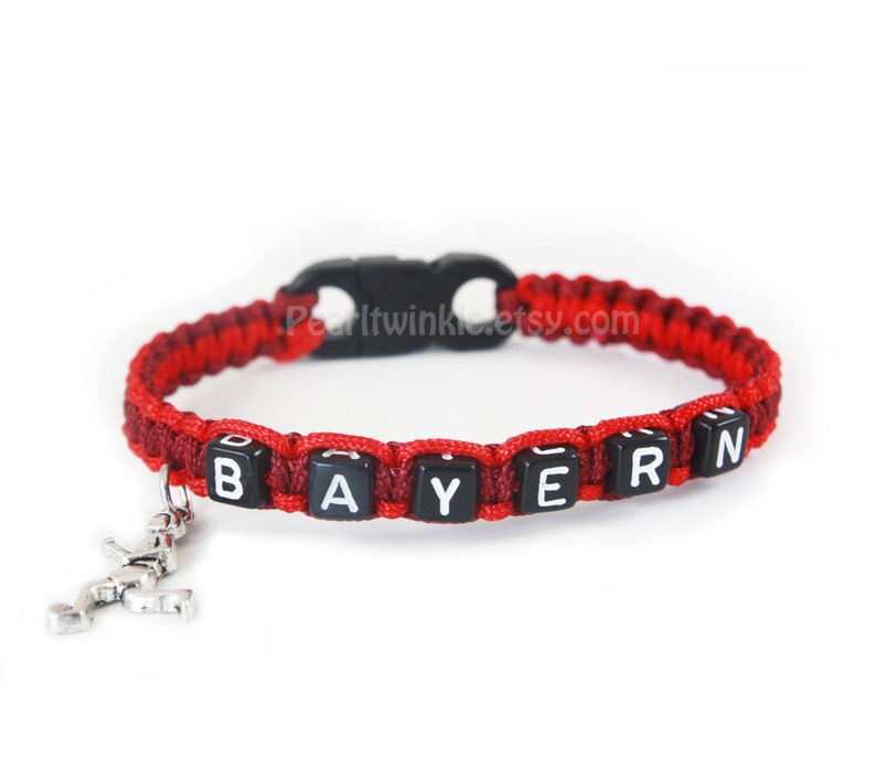 May include: Red and maroon braided bracelet with black beads spelling "BAYERN" and a silver charm of a football player.
